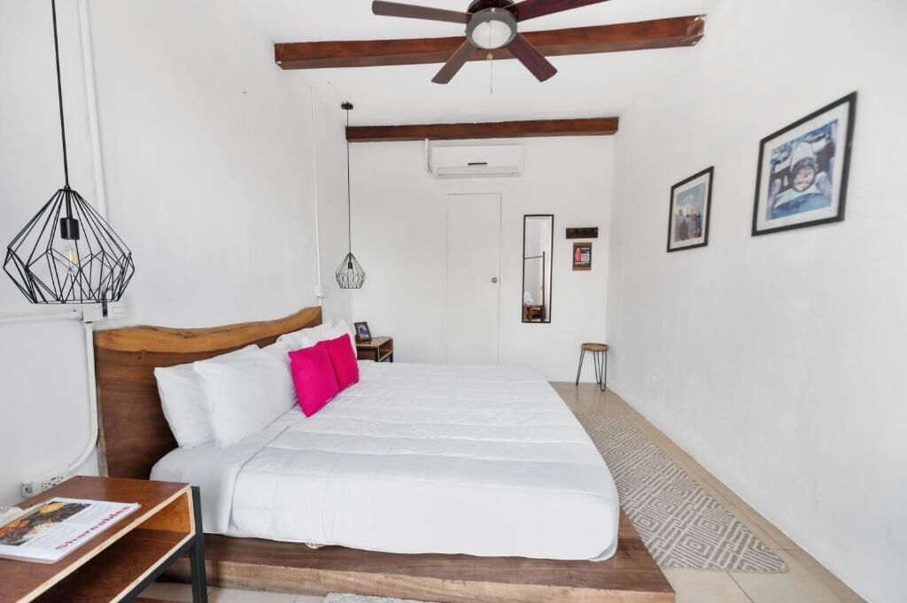 A bedroom with a wooden headboard, white bedding, a ceiling fan, and a patterned rug.