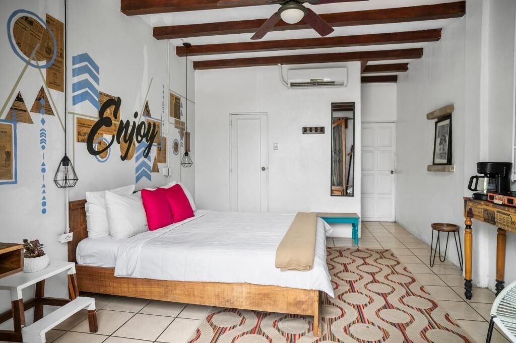 A bedroom with a bed, a desk, a chair, a ceiling fan, and a patterned rug.