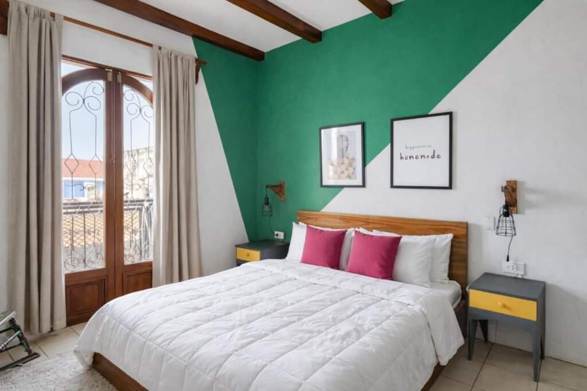 A bedroom with a bed, two bedside tables, a green accent wall, and a window with curtains.