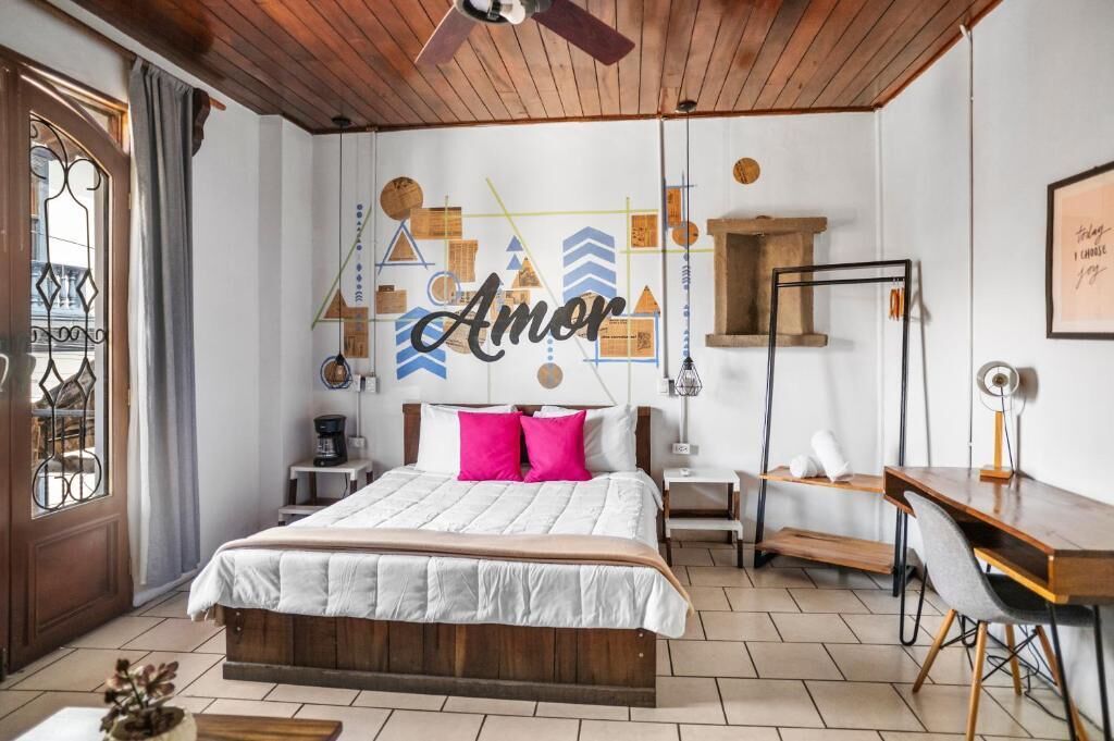 Quarto com cama, escrivaninha, cadeira e parede com formas geométricas e a palavra 'Amor'.