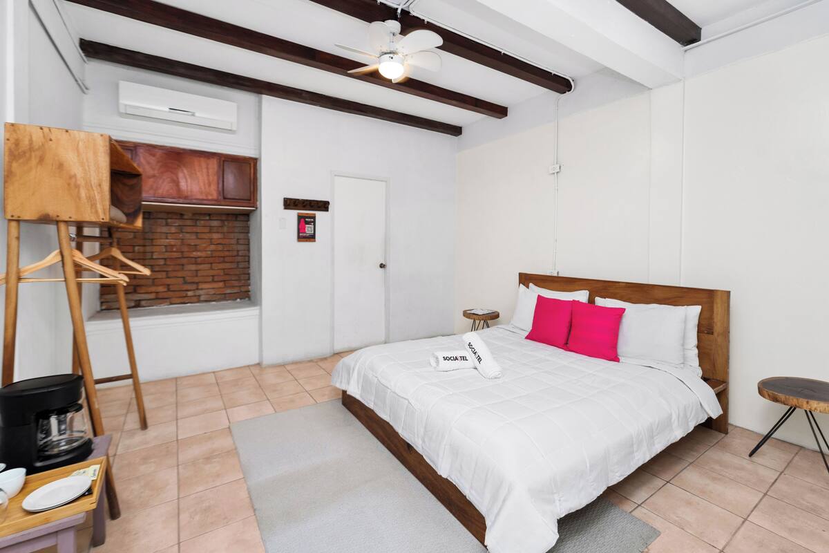 A hotel room with a bed, a wooden headboard, a hanging chair, a coffee maker, and a brick fireplace.