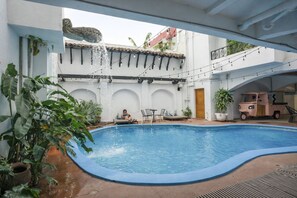 A swimming pool with a stone sculpture, outdoor seating, and a pink vehicle. - Socialtel Granada (Granada)