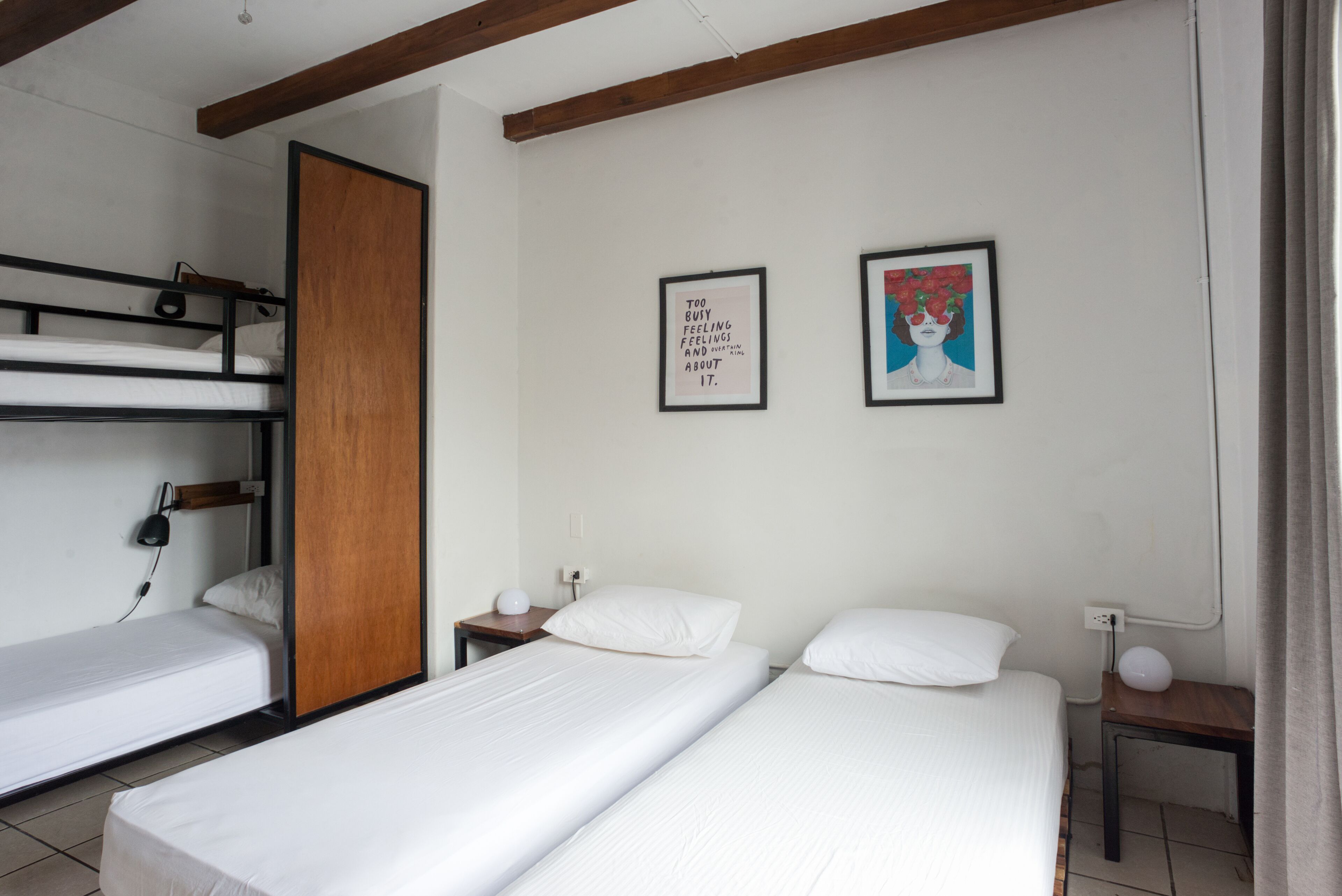Quarto com beliches, duas camas de solteiro, uma porta de madeira, uma mesa de cabeceira, uma luminária e duas fotos emolduradas na parede.