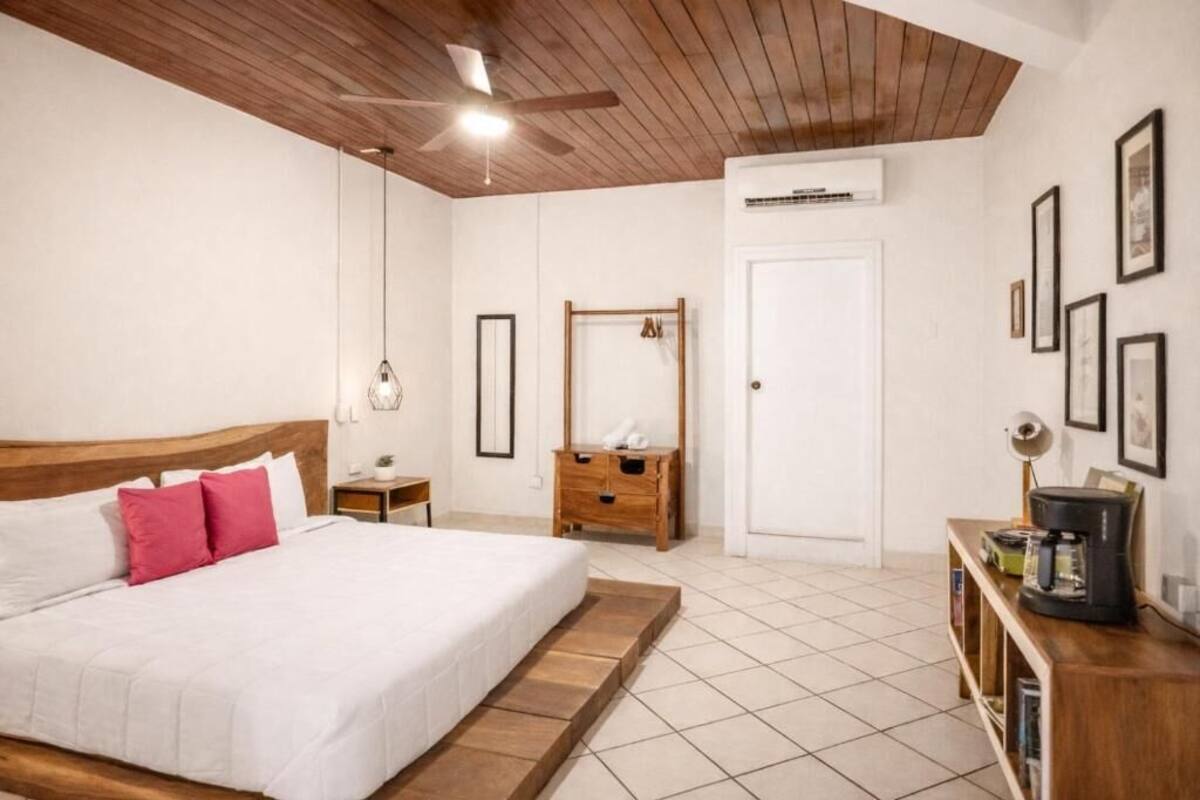 A bedroom with a bed, wooden headboard, bedside table, nightstand, dresser, and a coffee maker on a wooden side table.