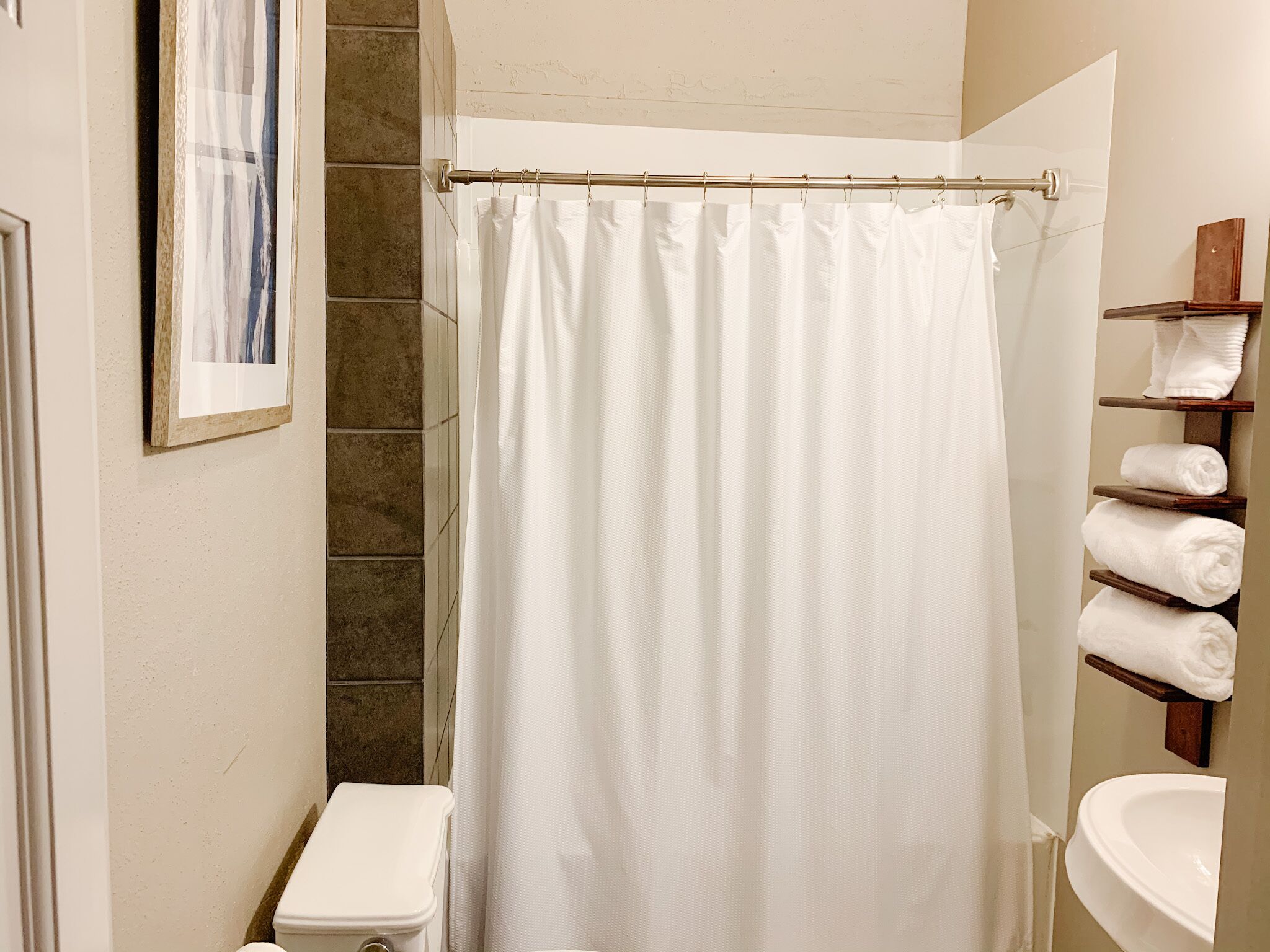 A bathroom with a white shower curtain, a toilet, and a sink with a towel rack.
