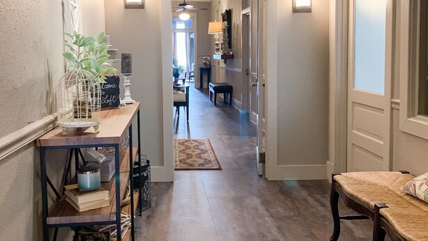 Un pasillo con un banco de madera, una mesa con adornos y una alfombra que conduce a una habitación con un piano.