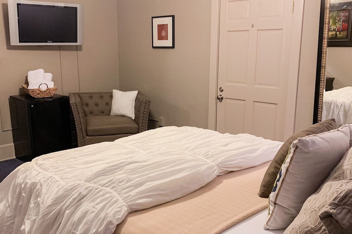 A hotel room with a bed, a television, a door, and a framed picture on the wall.