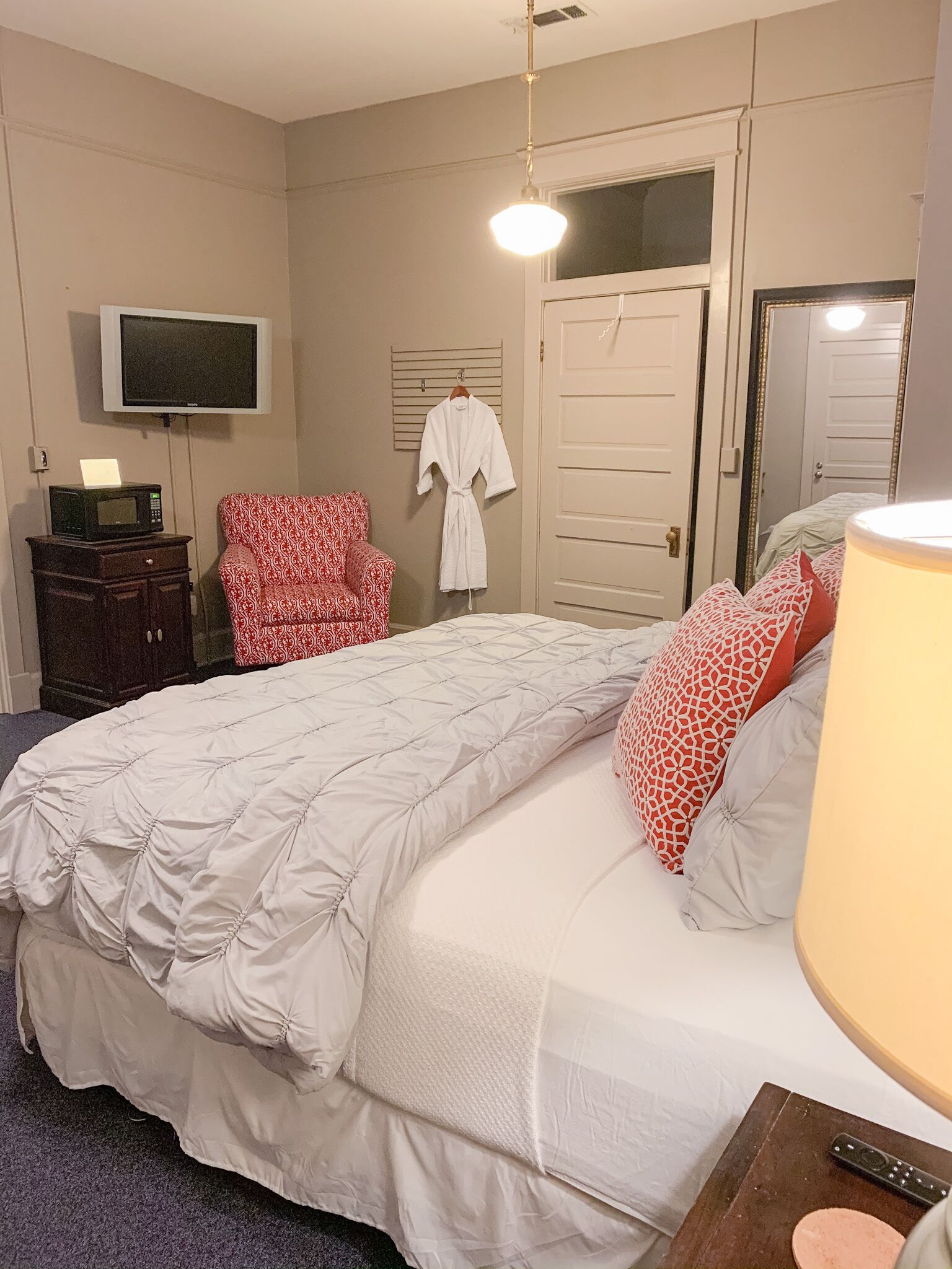 A bedroom with a large bed, a red patterned chair, a robe hanging on the wall, and a television mounted above the bed.