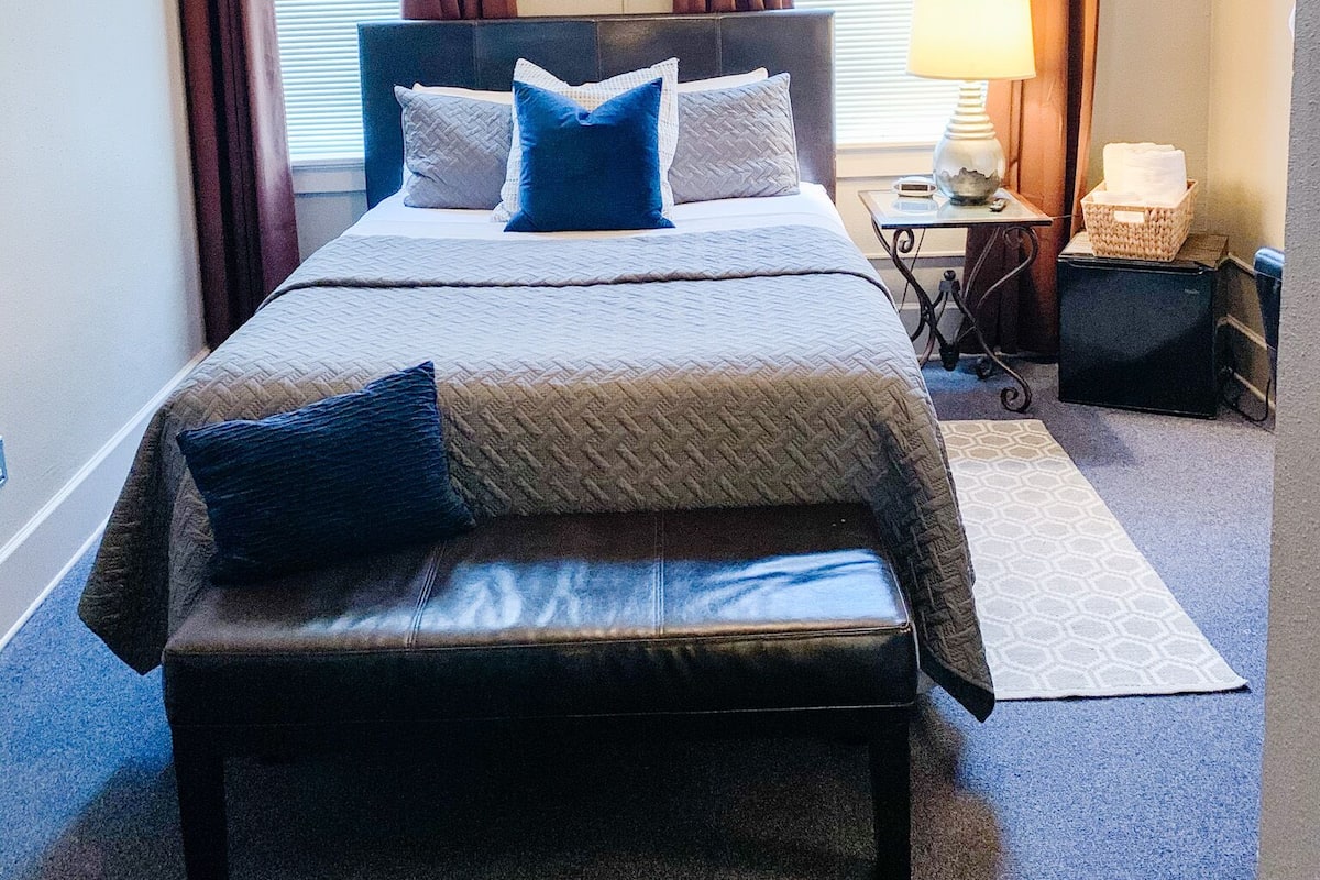 A neatly made bed with a headboard, a bedside table with a lamp, and a bench at the foot of the bed.