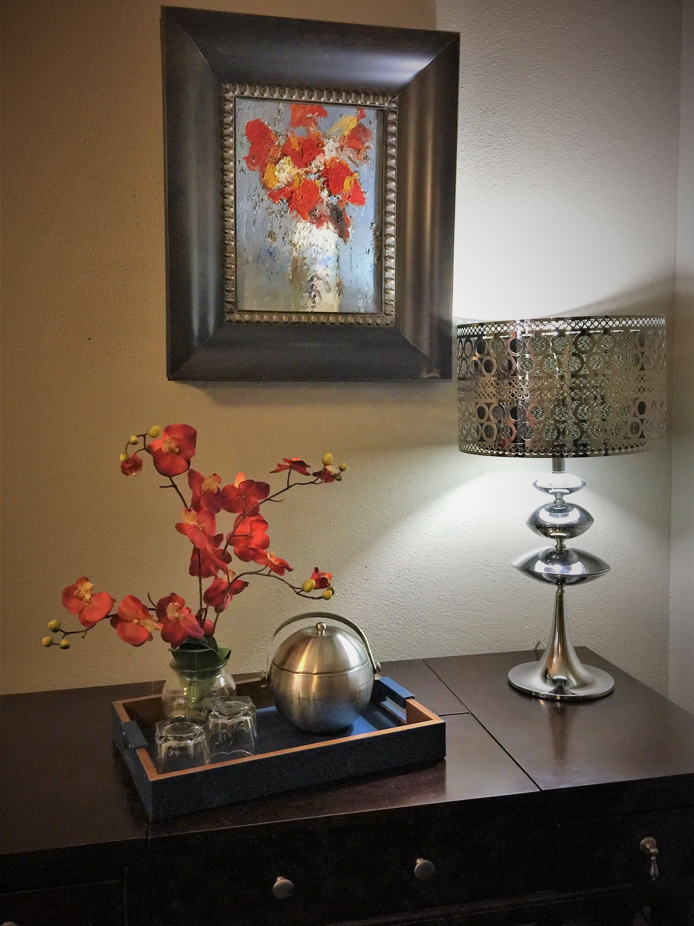 A table with a vase of flowers, a metal teapot, and a decorative lamp.