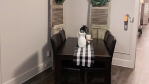 Un comedor con una mesa de madera oscura, dos sillas, una jarra blanca y una taza sobre un mantel a cuadros.