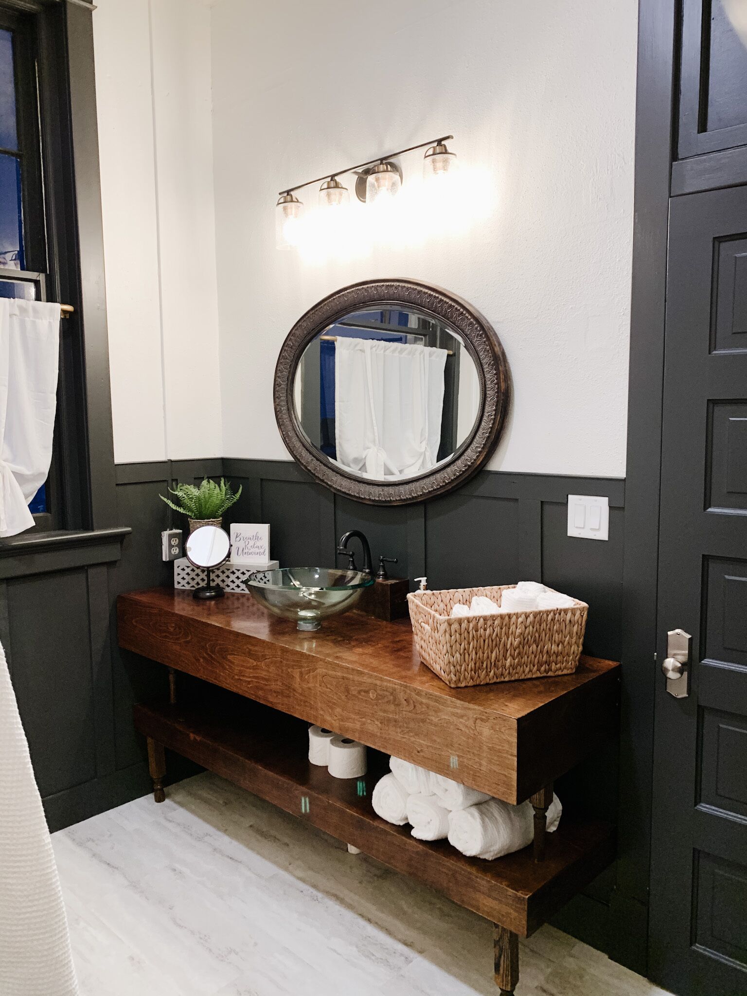 A bathroom with a wooden vanity, a round mirror, a glass bowl sink, and a towel rack.
