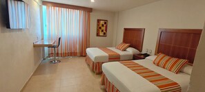 A hotel room with two beds, a desk, a chair, and a TV.