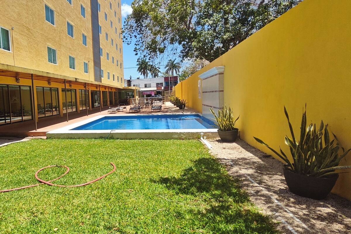 A courtyard with a swimming pool, a grassy area, and a yellow building with large windows.