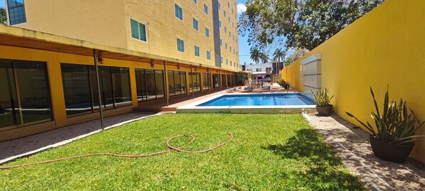 A courtyard with a swimming pool, a grassy area, and a yellow building with large windows.