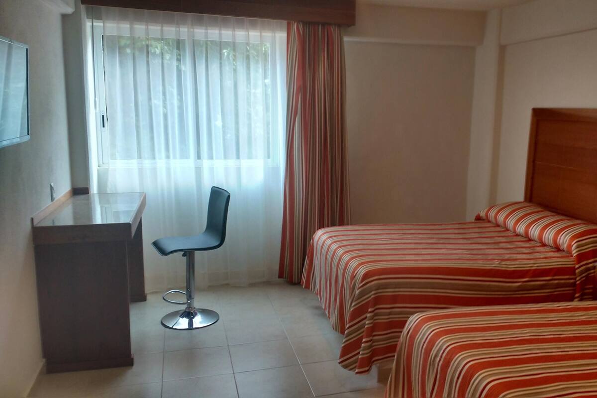 A hotel room with two beds, a desk, and a chair.