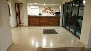 A hotel reception area with a wooden counter, a reception desk, and a glass door leading to a parking area. - Misol-Ha Hotel Mérida (Mérida)