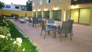 An outdoor patio area with tables and chairs, a small garden with white flowers, and a building with glass doors and windows. - Misol-Ha Hotel Mérida (Mérida)