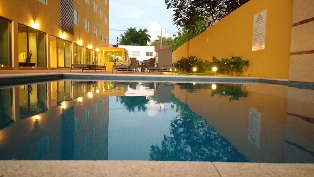 A swimming pool with a reflection of the surrounding buildings, a seating area with chairs, and a well-lit outdoor space. - Misol-Ha Hotel Mérida (Mérida)