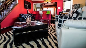 Ein Wohnzimmer mit roter Wand, Hocker in Schwarz, einer weißen Couch und einer Chandelüster.