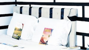 Ein Bett mit grau und weiß gestreifter Kopfteil, zwei Kissen und eine Zeitschrift darauf.