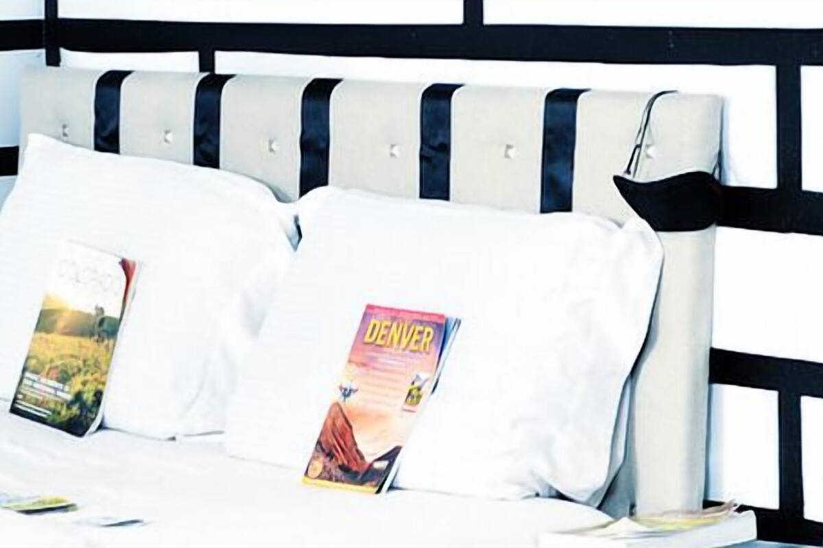 Una cama con cabecera negra y blanca, dos almohadas y una revista sobre la cama.