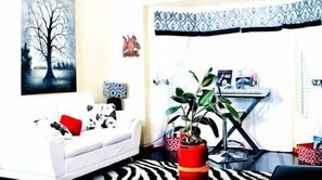 A living room with a white sofa, a red and black patterned rug, a potted plant, and a desk with a computer.