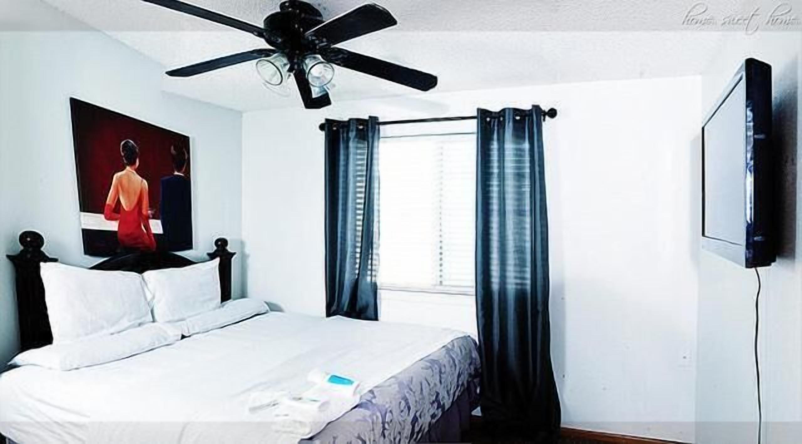 A bedroom with a bed, a ceiling fan, a TV, and curtains.
