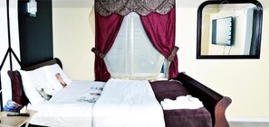 A hotel room with a bed, a chair, a nightstand, and a window with curtains.