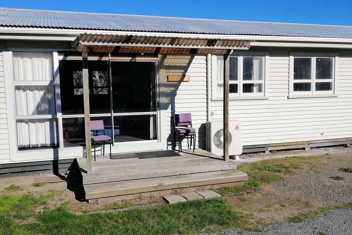 A single-story house with a covered porch, a sliding glass door, and a small outdoor seating area with two chairs.