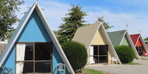 A row of triangular A-frame cabins with sliding glass doors and white plastic chairs outside.