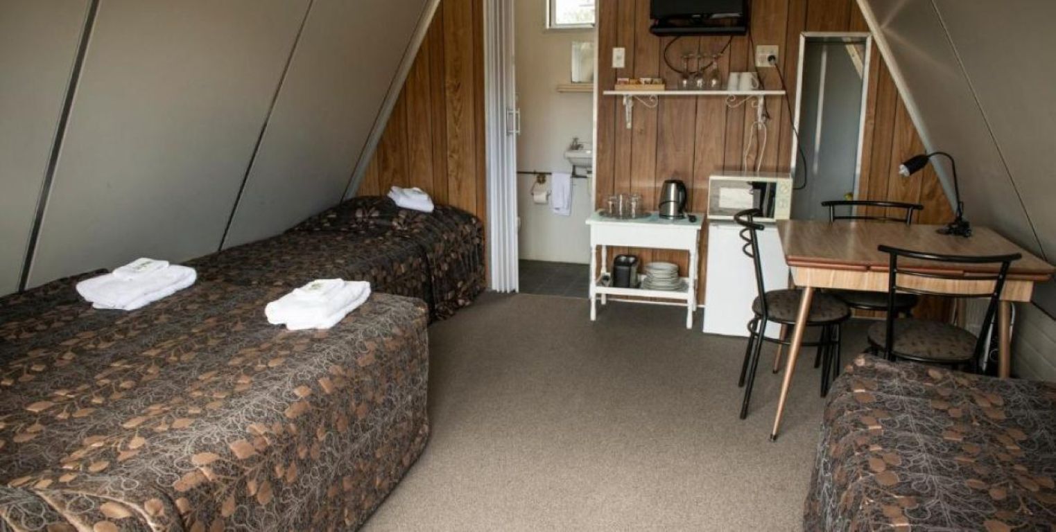 Une chambre de taille modeste, équipée de deux lits, d’un petit bureau, d’une chaise et d’un téléviseur.