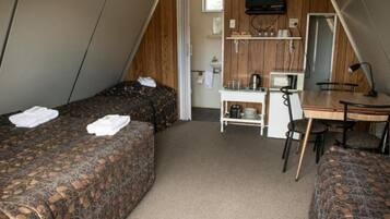Une chambre de taille modeste, équipée de deux lits, d’un petit bureau, d’une chaise et d’un téléviseur.