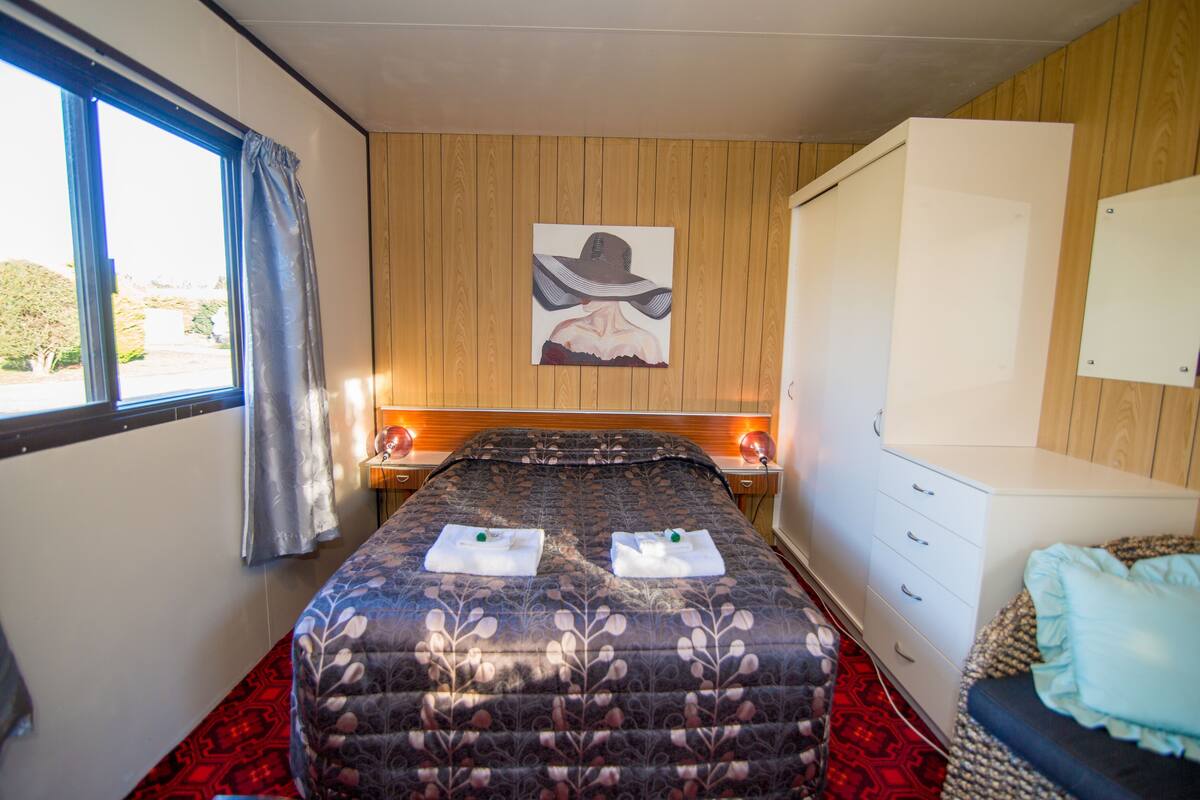 A bedroom with a bed, a nightstand, a dresser, and a window with curtains.