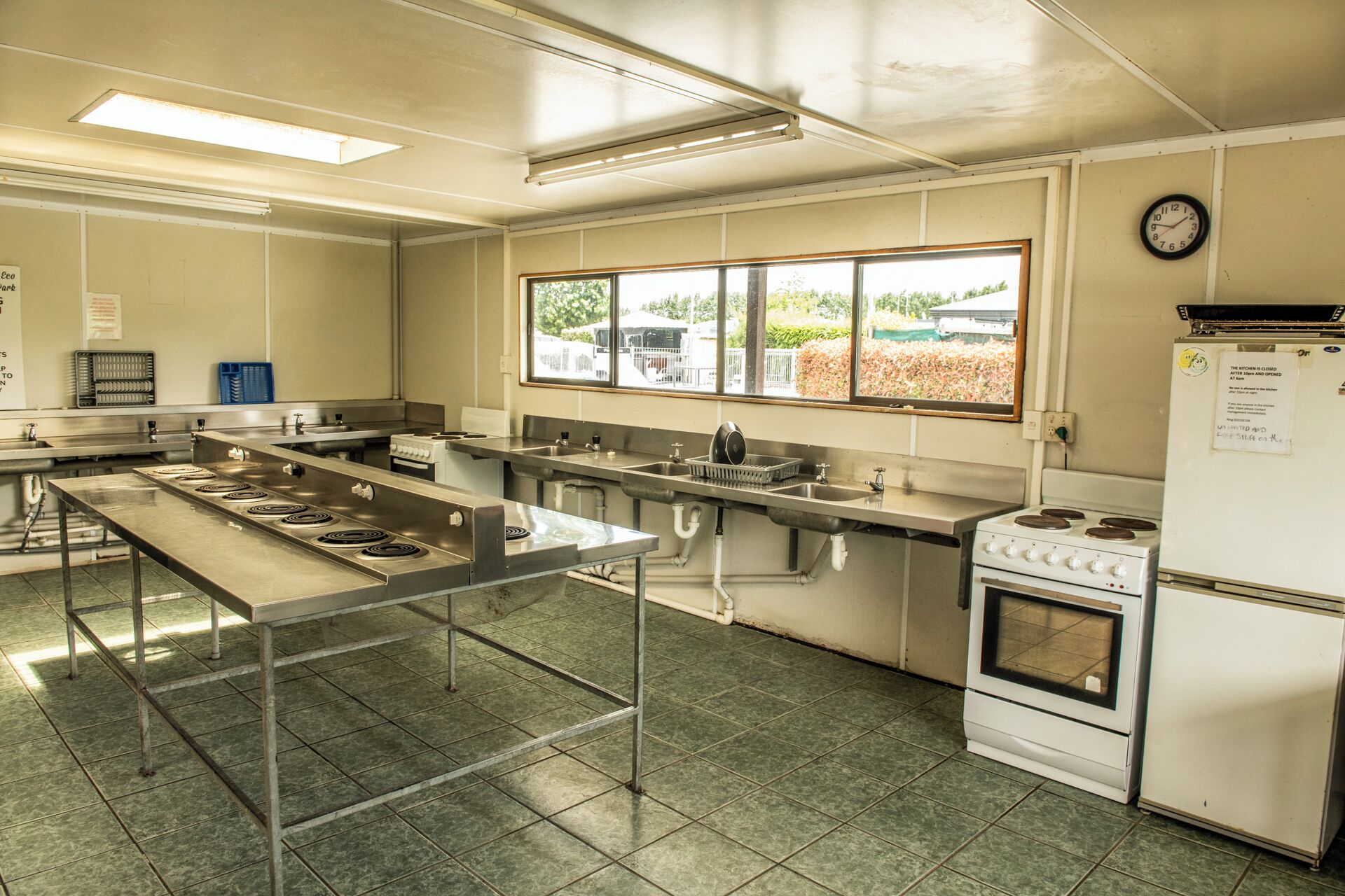 A commercial kitchen with stainless steel appliances, a large central island, and a view through the windows.