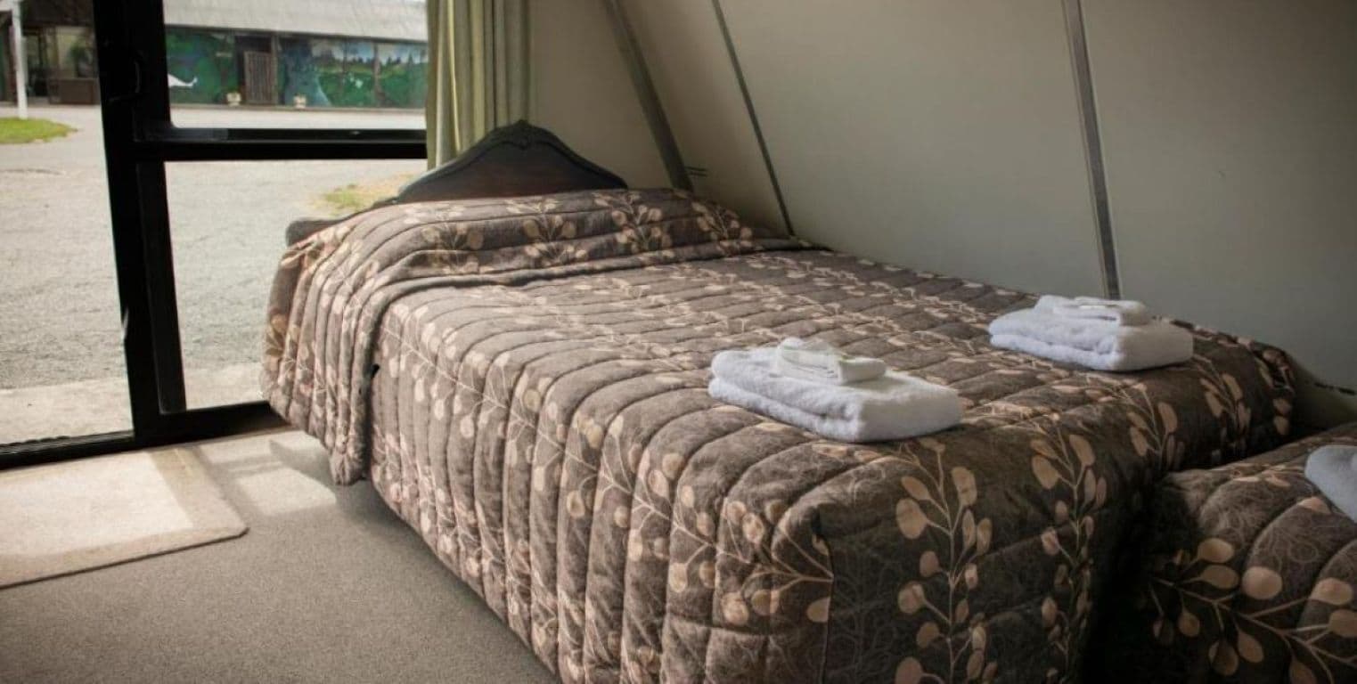 Una cama individual con una colcha de estampado floral y dos toallas dobladas con cuidado.