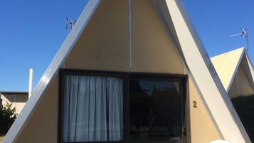 Un edificio triangular con un amplio ventanal corredero, dos sillas de plástico blanco y el número 2 en la puerta.