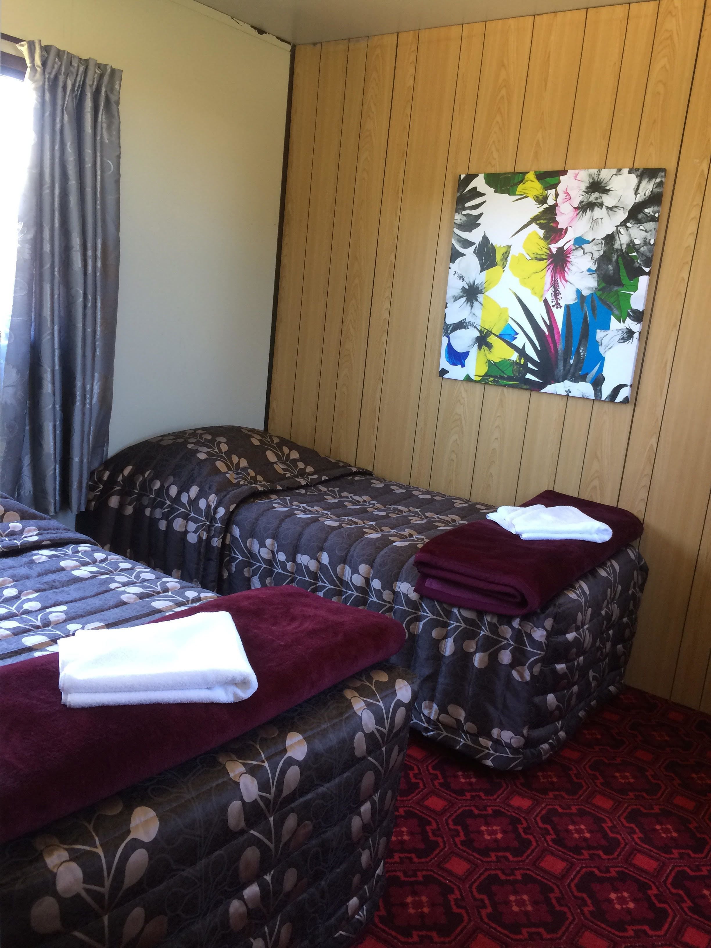 A hotel room with two beds, a wooden panel wall, and a floral painting.