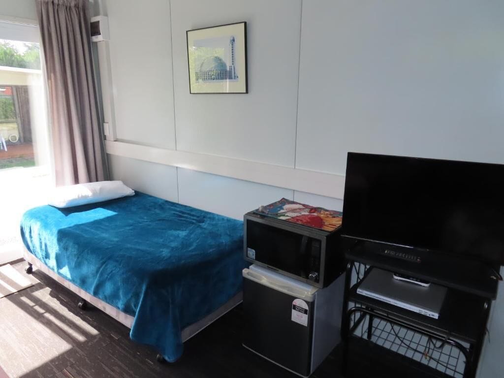 Una habitación de hotel con cama, televisión, refrigerador pequeño y ventana con cortinas.