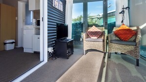 Una habitación con televisión, una kitchenette pequeña y un sillón de mimbre con cojines.