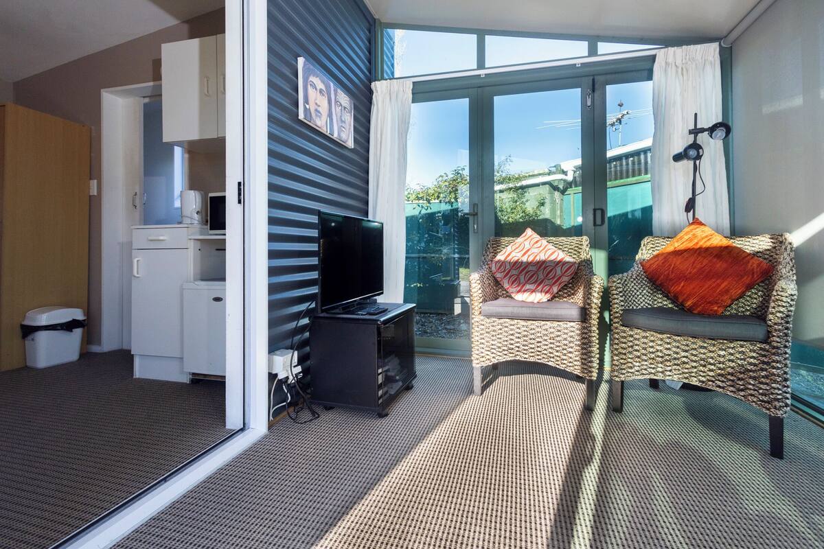 A room with a television, a small kitchenette, and a wicker chair with cushions.