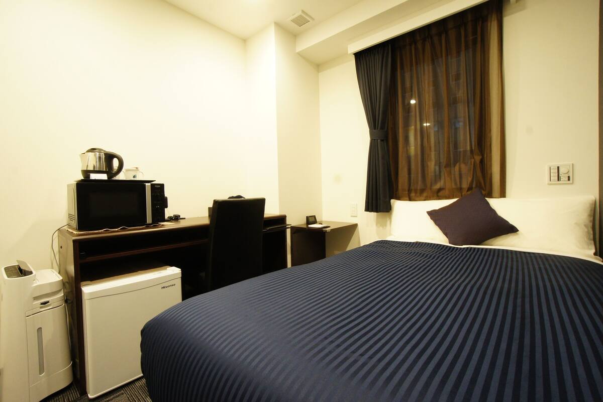 Una habitación de hotel con cama, escritorio con computadora, microondas y refrigerador pequeño.