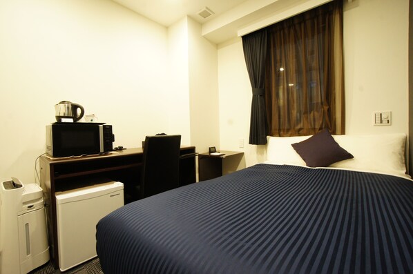 A hotel room with a bed, a desk with a computer, a microwave, and a small refrigerator.