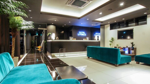 A hotel lobby with teal sofas, a reception desk, and a TV screen. - Hotel LiVEMAX Nagoya Sakae East (Nagoya)