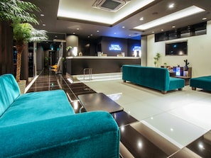 A hotel lobby with teal sofas, a reception desk, and a TV screen.