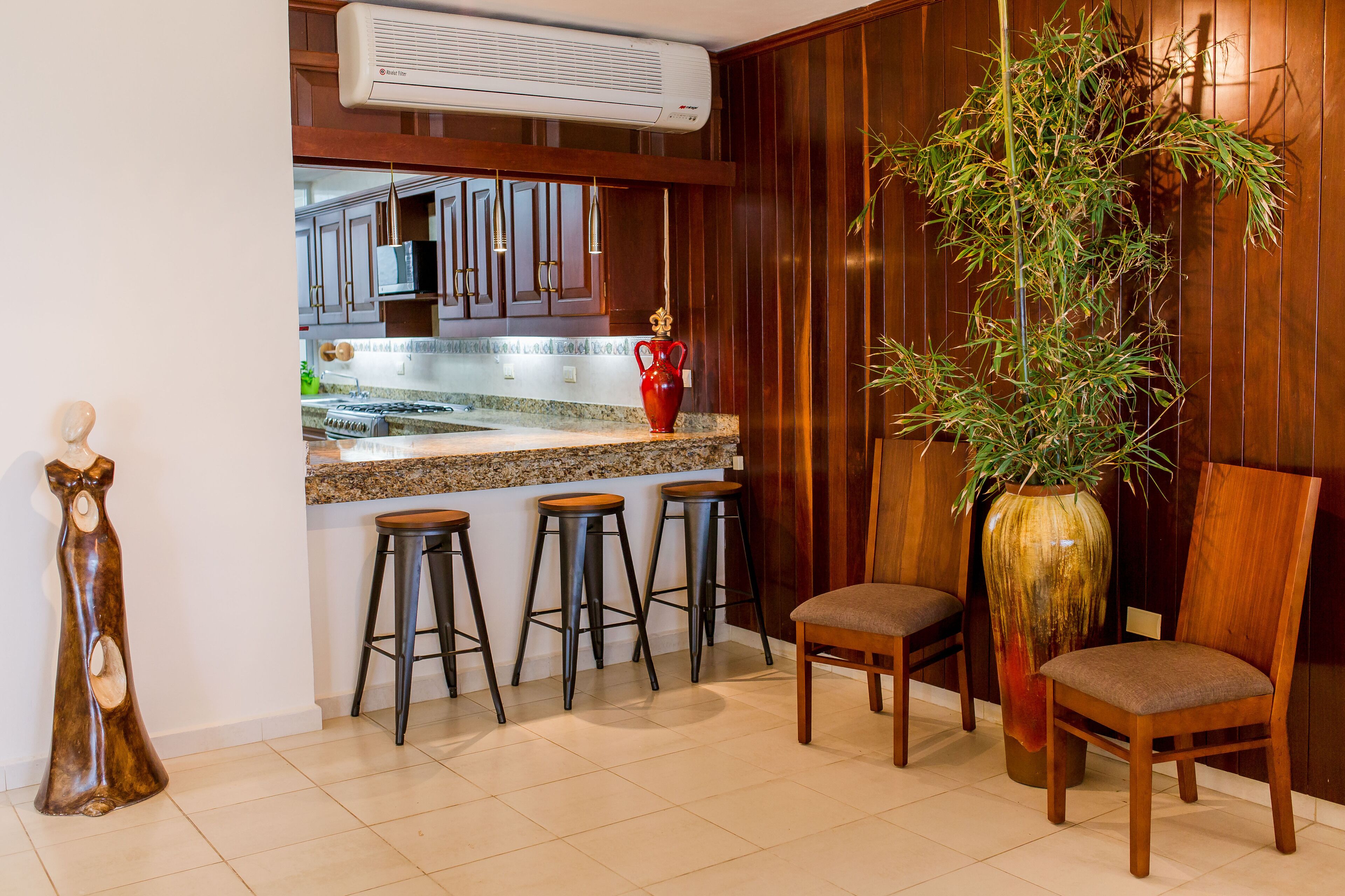 A kitchen with a wooden bar, stools, a large vase, and a chair.