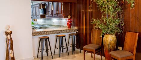 A kitchen with a wooden bar, stools, a large vase, and a chair.