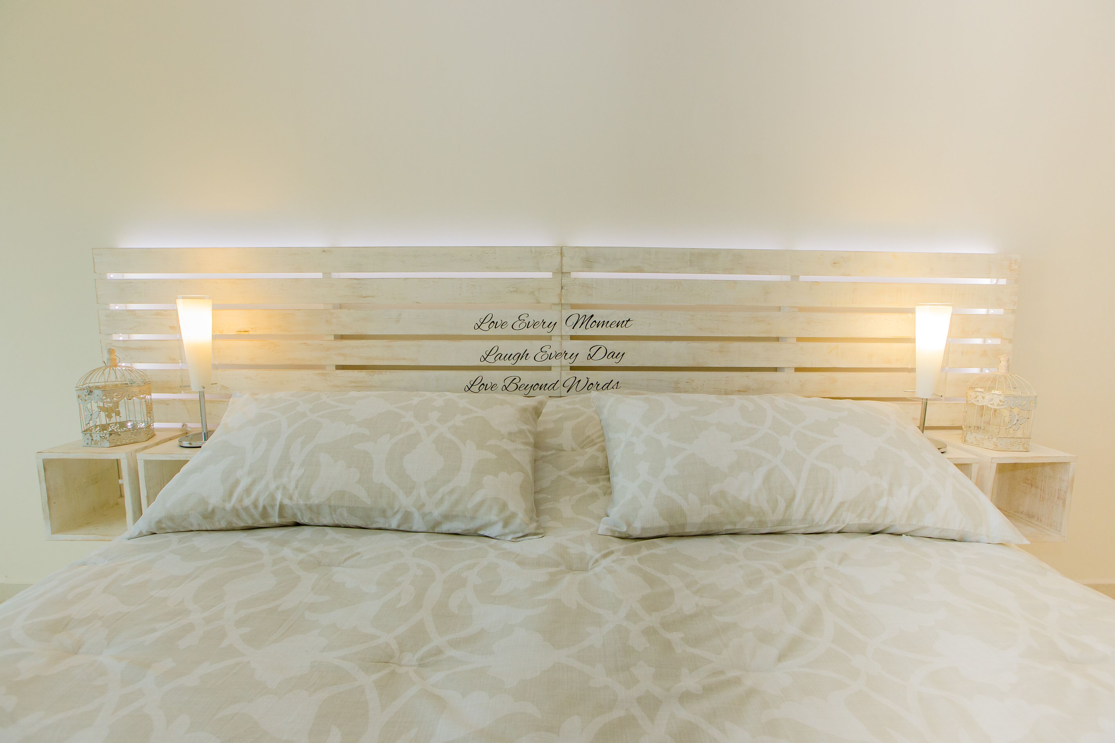 A bed with a headboard displaying inspirational phrases, flanked by two bedside tables with decorative items.
