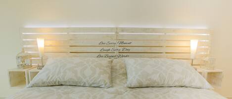 A bed with a headboard displaying inspirational phrases, flanked by two bedside tables with decorative items.
