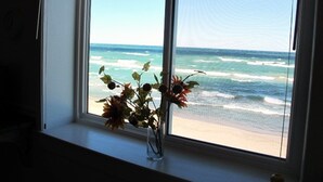 Una ventana con vista al océano y un florero con flores en el alféizar.